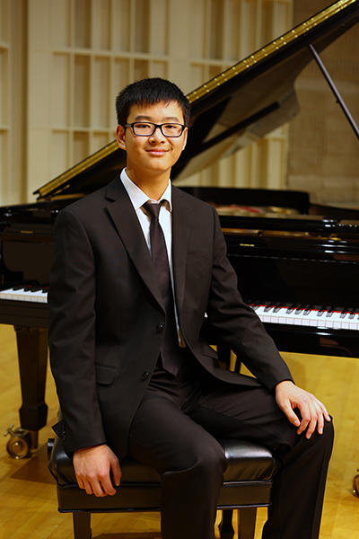 Henry Shao competition winner sitting on stage in front of a piano