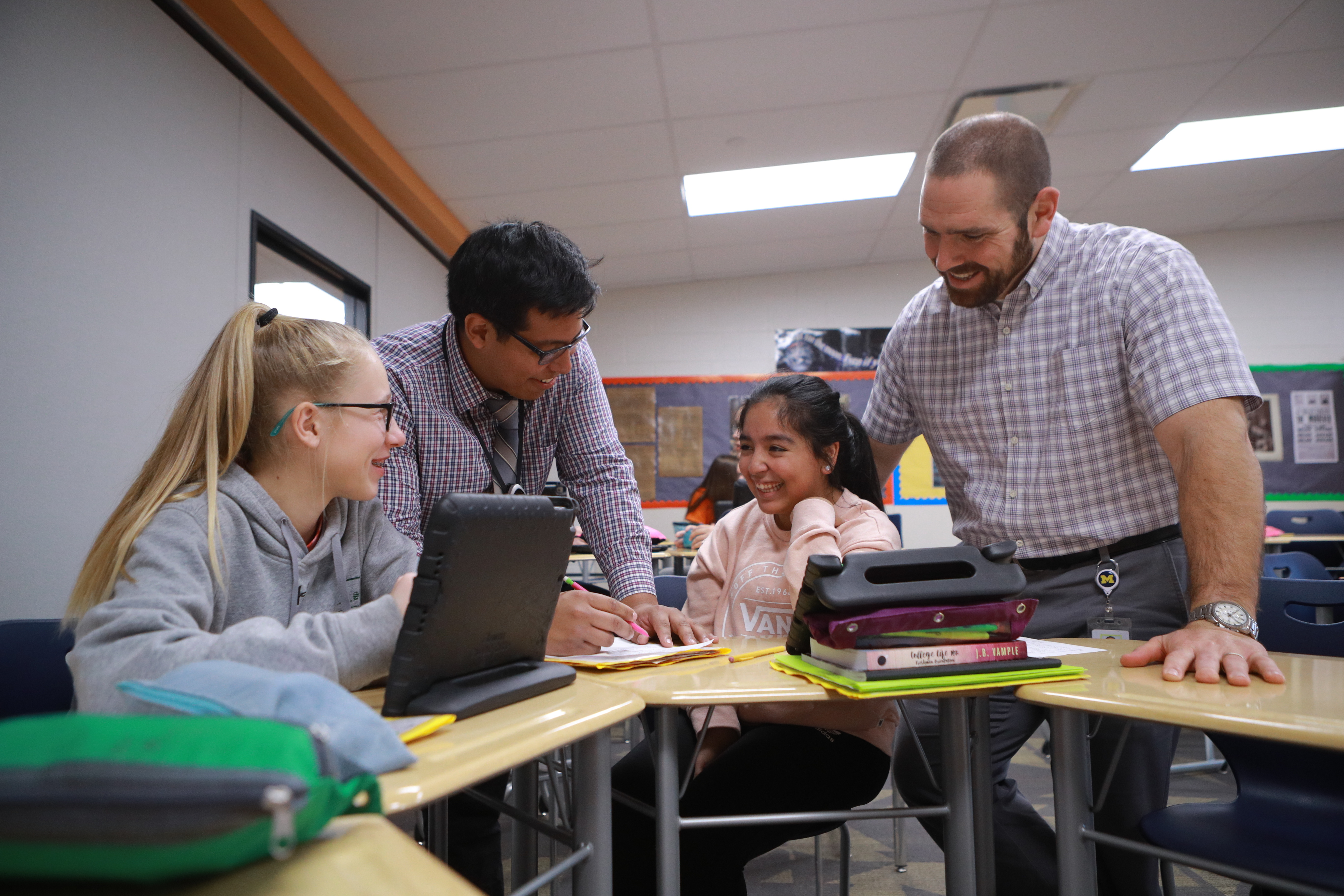 two students seated at their desks interacting with two teachers