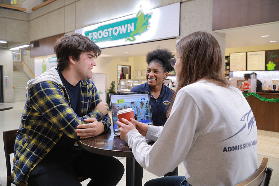 Three people chat at a table, with a laptop and red to-go cup in front of Frogtown