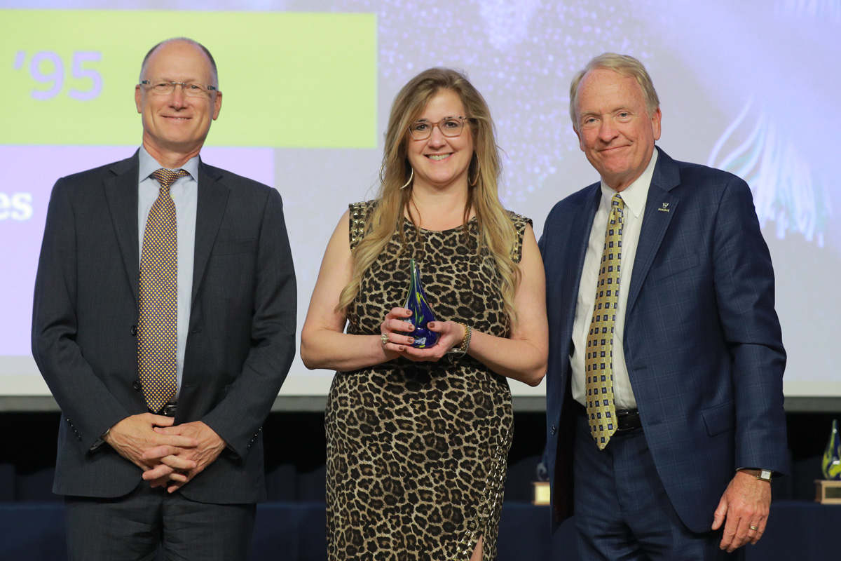 Our Distinguished Alumni Recipient Dr. Jennifer Christner stands with her award in between Dean Cooper and President Postel at the 2023 Homecoming Gala. 