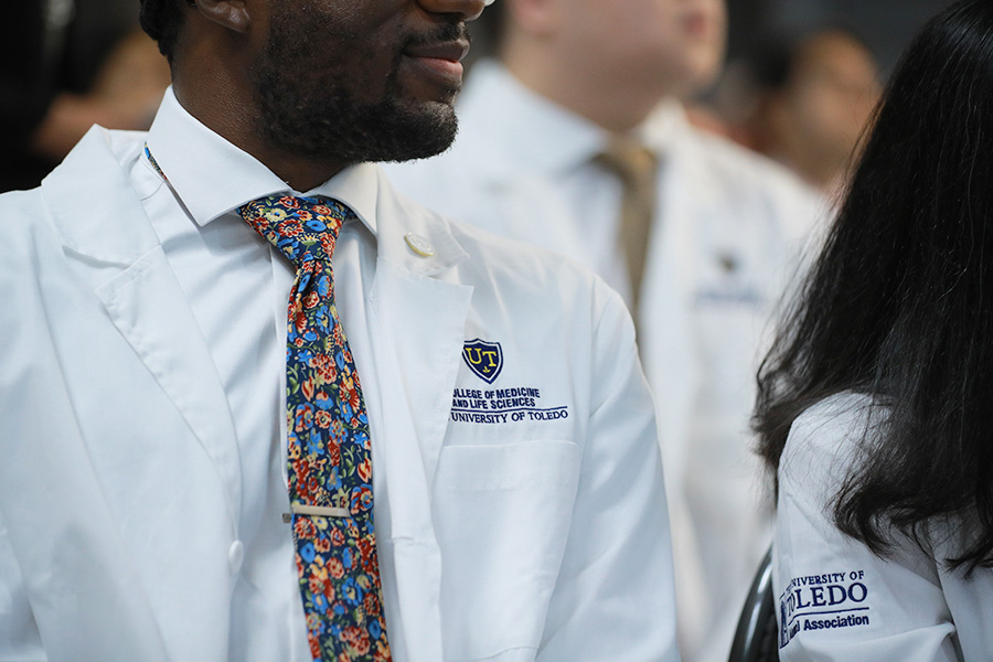 Student wearing a blue tie and white coat with an University of Toledo College of Medicine and Life Sciences logo embroidered on it