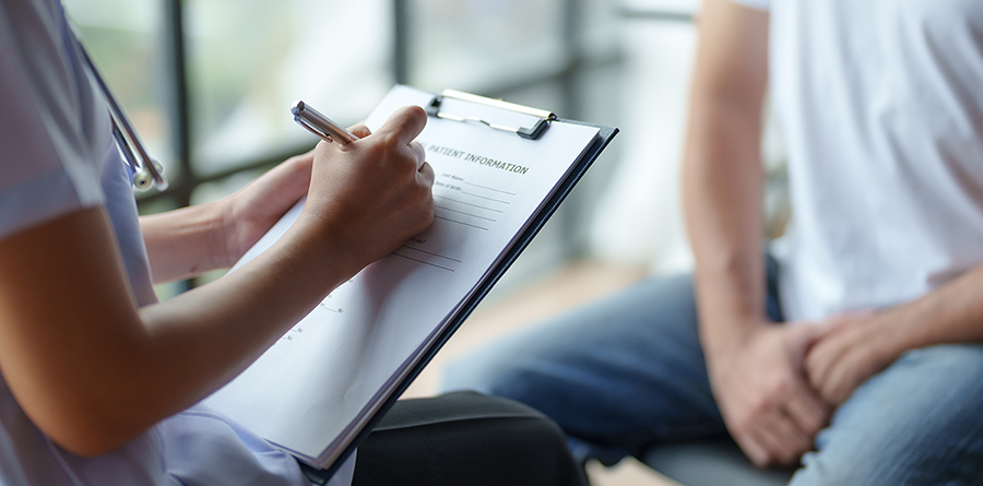 Stock photo of a healthcare professional taking notes during a patient consultation, focused on providing medical care and support in a clinical setting.