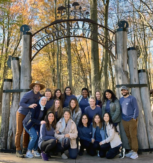 Resident at a retreat in front of a sign for the treehouse village