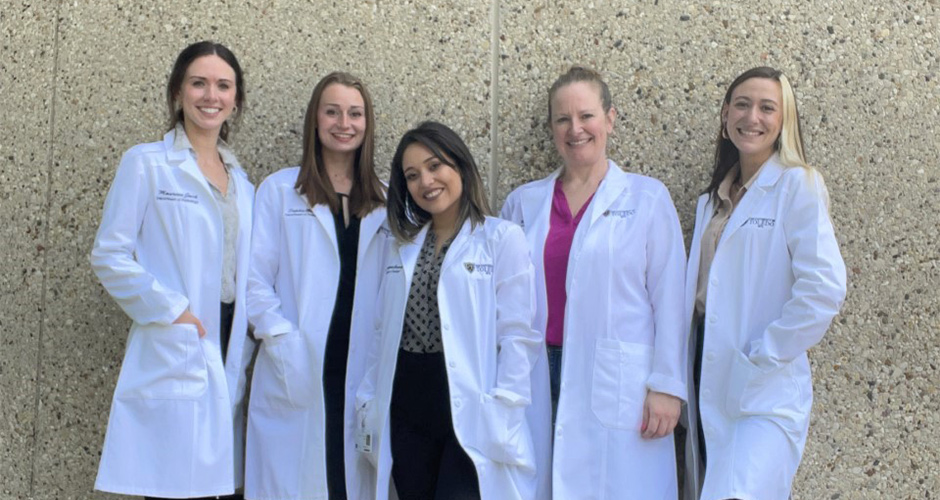 Students pose for a photo in their white coats.