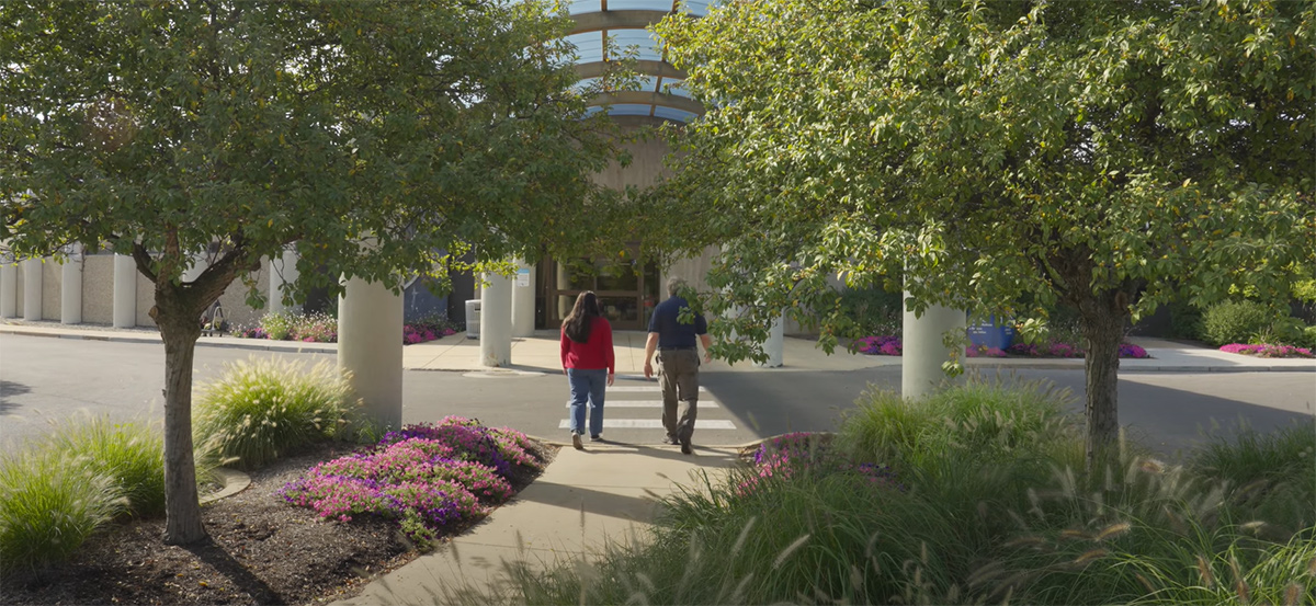Two people walking into a clinic on Health Science Campus featuring lush greenery.