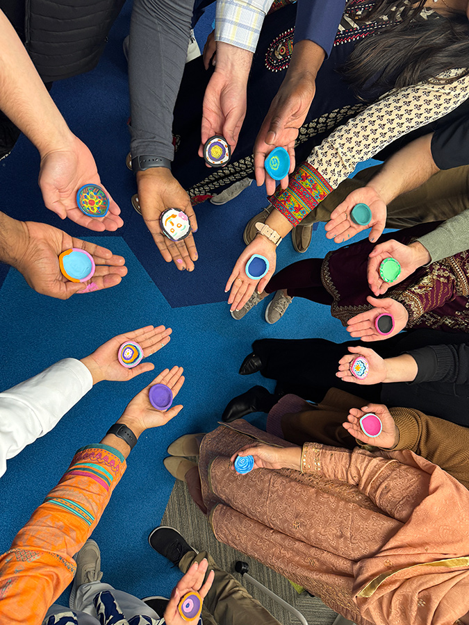 A group of people stand in a circle, each holding a small, colorful circular item in their hands, highlighting a shared activity or cultural exchange.
