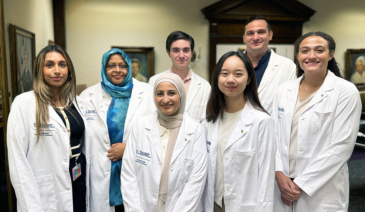 A group of medical residents in white coats stand together indoors, smiling for a group photo in a formal setting.
