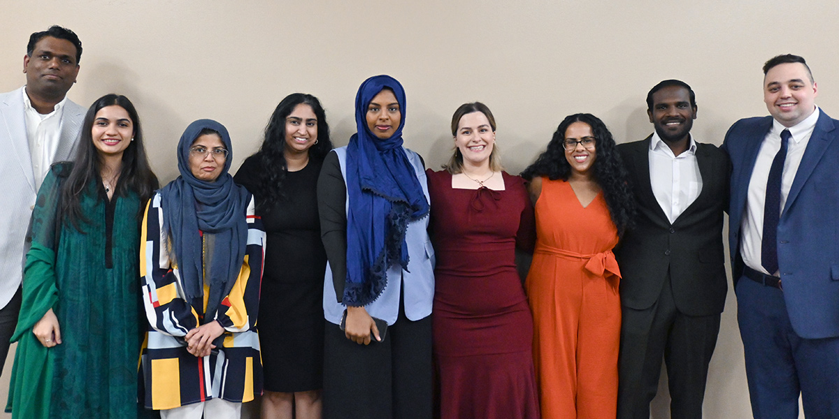 A group of medical residents stand side by side against a neutral wall, dressed in professional attire and smiling for a group photo.