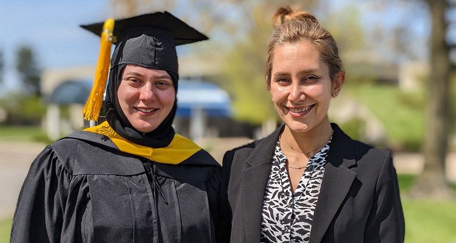 Two people pictured outside, one wearing a graduate cap and gown