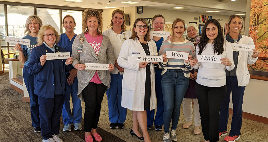 Women from the division hold up signs #WomenWhoCurie