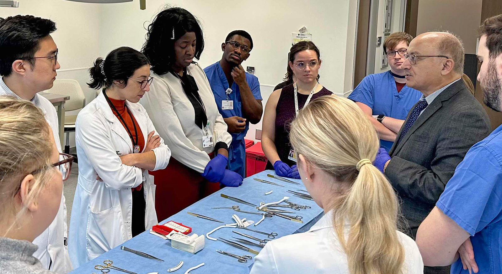 Surgery residents in the Simulation Center around a table listening to a faculty member.