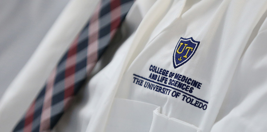A student wears a white coat and a tie.