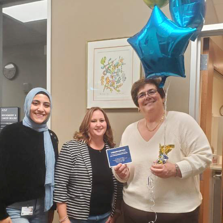 Two representatives from HR personally stopped by the department to notify Jenny Zak that she was selected for this award. Jenny is holding balloons and a congratulation notecard.