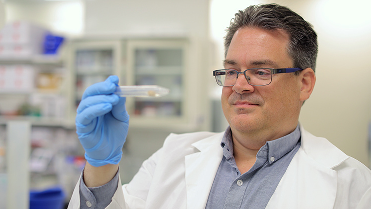 Photo of Dr. James Burkett, a neuroscientist and assistant professor in the Department of Neurosciences and Psychiatry, looking at a syringe.