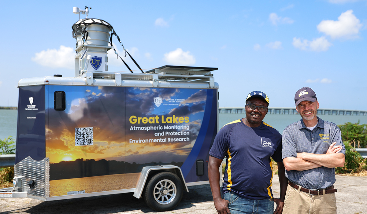 Dr. Kennedy Doro and Dr. David Kennedy stand in front of UToledo's trailer-mounted atmospheric sampling platform at the Lake Erie shoreline.