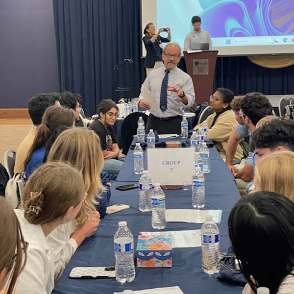 Dr. Kris Brickman speaks to students who are seated at a long table during the IPE Kickoff event. 