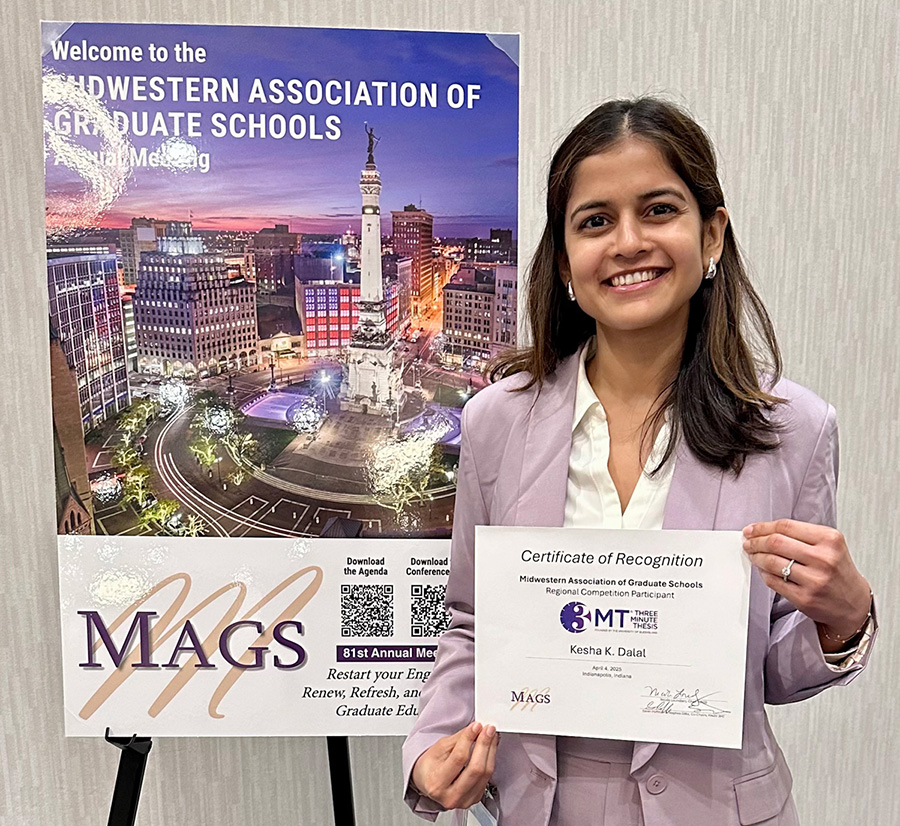 Student Kesha Dalal holds a certificate of recognition while standing in front of a poster for the regional 3-Minute Thesis (3MT) competition, held in Indianapolis by the Midwest Association of Graduate Schools (MAGS).