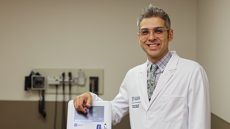 Dr. Mani Askari poses with an automated machine that can take blood pressure measurements without a medical professional in the room.