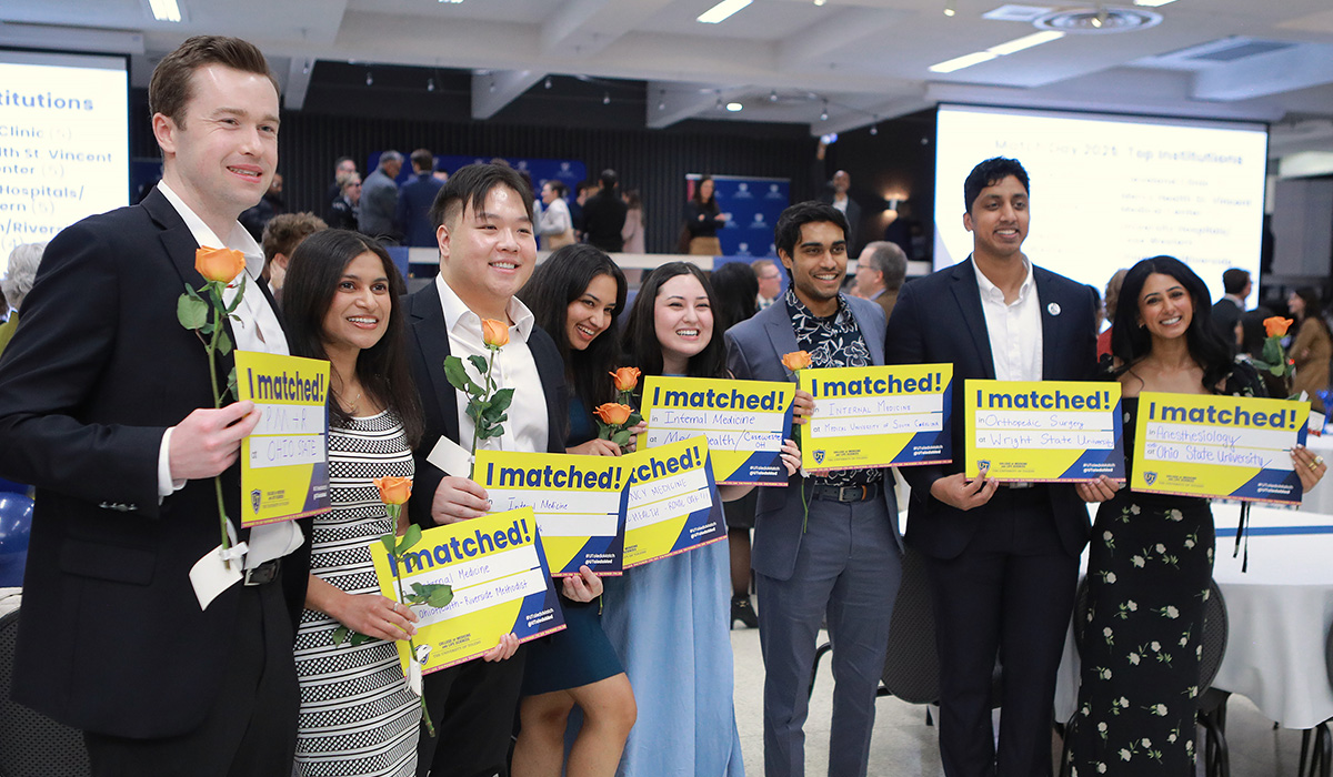 Eight students stand for a group photo while holding their Match signs. Many are also holding roses. 