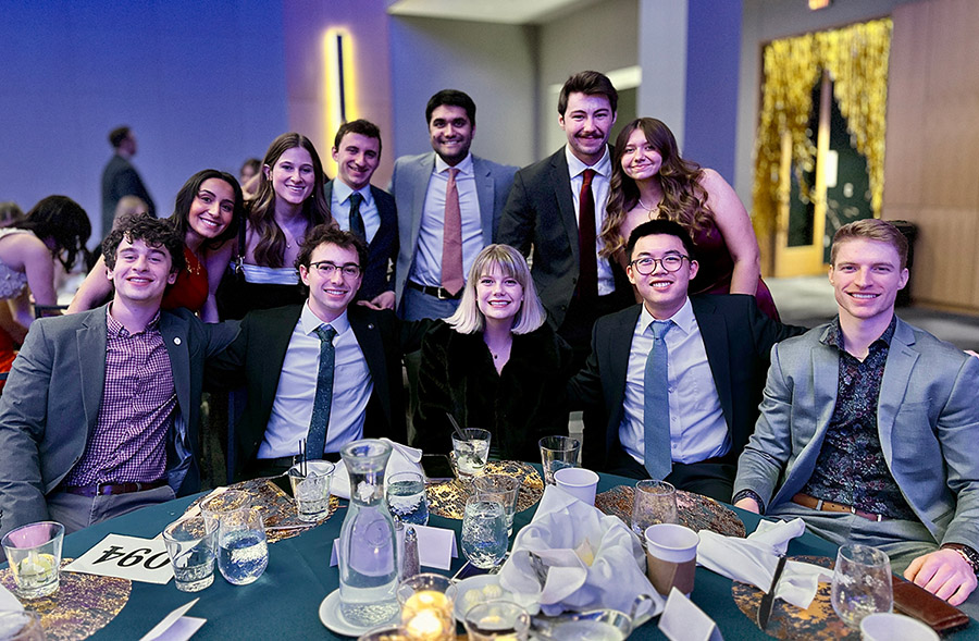 A group photo from Medicine Ball featuring attendees sitting at table with several standing behind them.