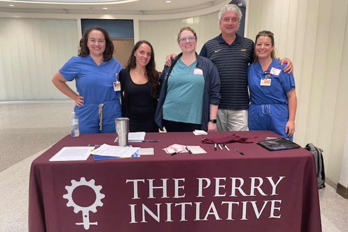 Organizers are pictured inside the Simulation Center in the atrium, beyond a table with The Perry Initiative logo. 