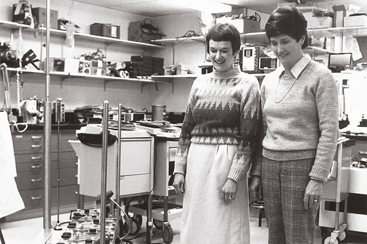 Archive black and white photo of two Satellites members viewing a heart-lung machine purchased for the hospital with funds from the organization.