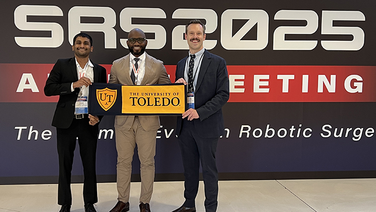 Second-year medical students Tarak Davuluri, left,and Paul Gabriel, right, traveled to France with Dr. Obi Ekewenna, center, last month to present research on artificial intelligence in patient education. The three are holding a University of Toledo sign.