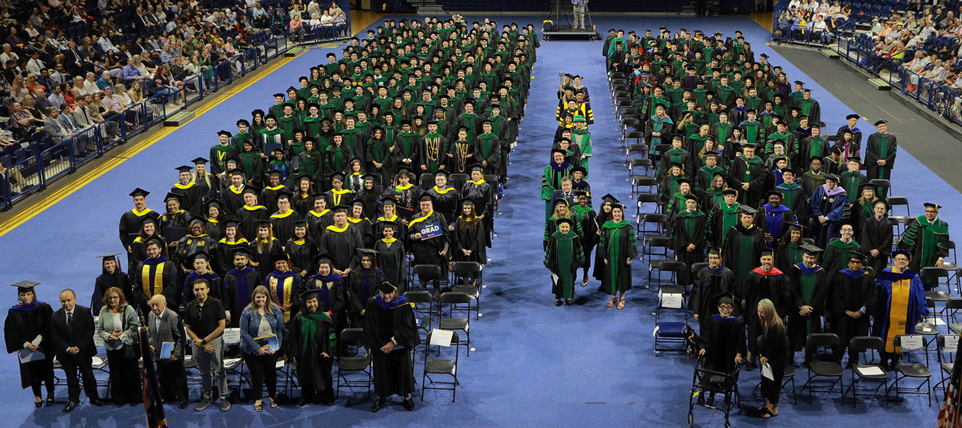 The Class of 2025 is pictured on the left with faculty on the right on the floor of Savage Arena during the 54th Commencement Exercises. 