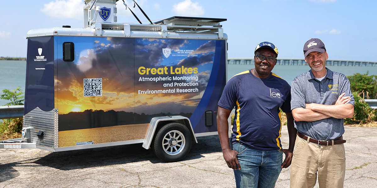 Dr. Kennedy Doro and Dr. David Kennedy stand in front of UToledo's trailer-mounted atmospheric sampling platform at the Lake Erie shoreline.