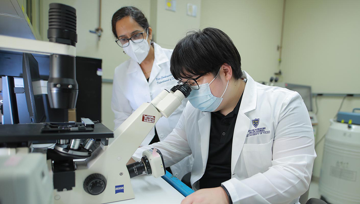 Student looks into microscope while being supervised by a faculty member.