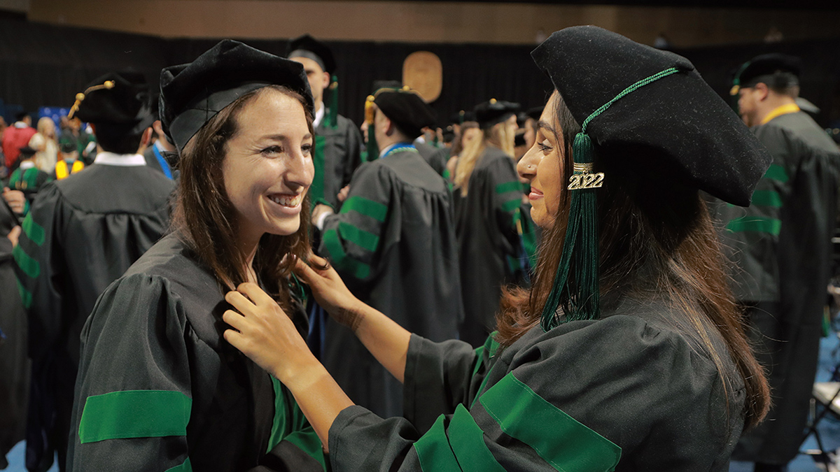 One graduate assists another with her hair before commencement begins
