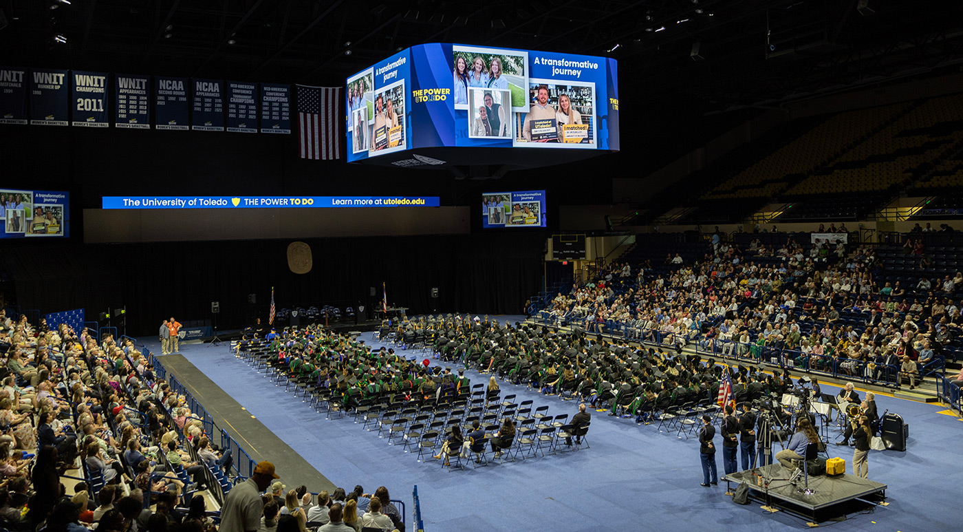 Photo of Savage Arena with students seated on the floor. On the video board is a photo collage with text: A transformative journey. 