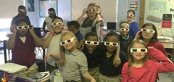 group of elementary students in a classroom with their teacher wearing 3D glasses