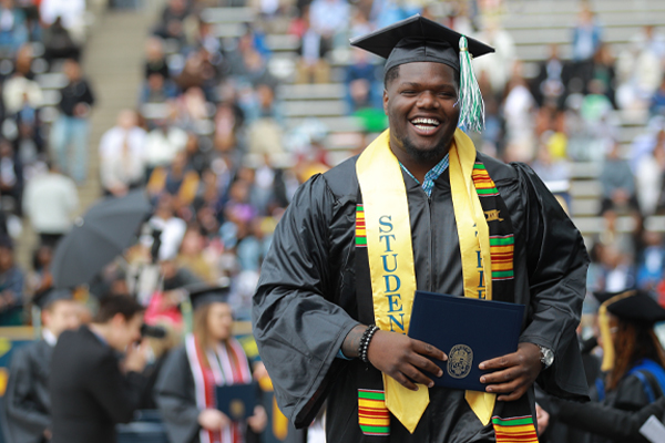 A graduate from the College of Health and Human Services smiles widely as he walks with his new diploman at commencement 