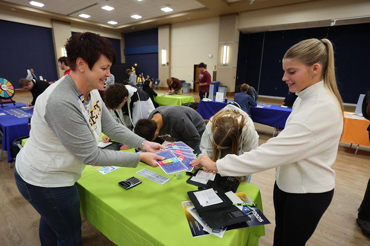 two women standing up smiling and playing cards that say finance 101