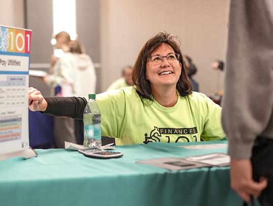 woman at financial wellness fair seated at booth with a spinning wheel