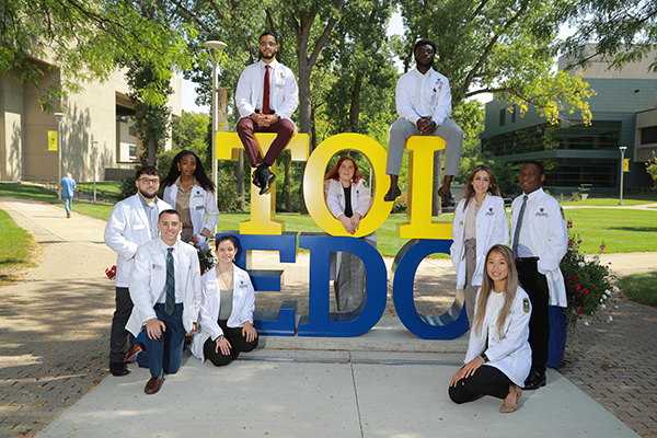 Pharmacy students standing around the UToledo letters sign