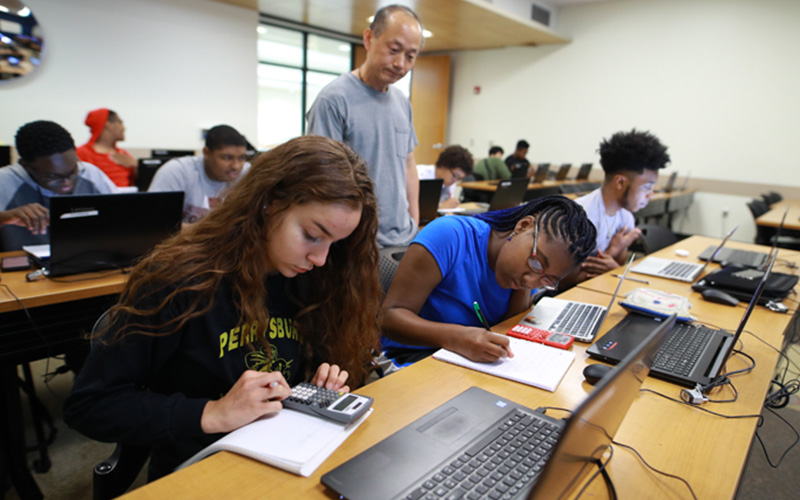 Students working with laptops and calculators in a classroom
