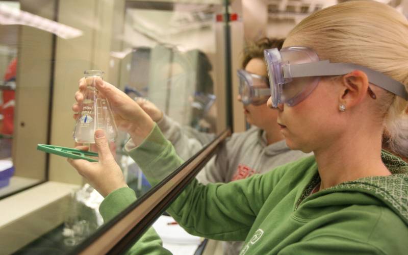 students in a lab wearing goggles and holding a beaker containing liquid