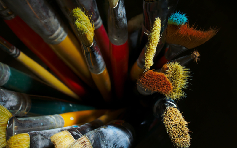 close up image of used paint brushes coated in various colors of paint