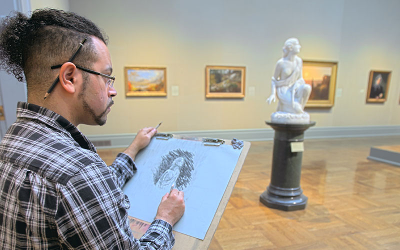 man at an easle stand studies and sketches the statue in front of him