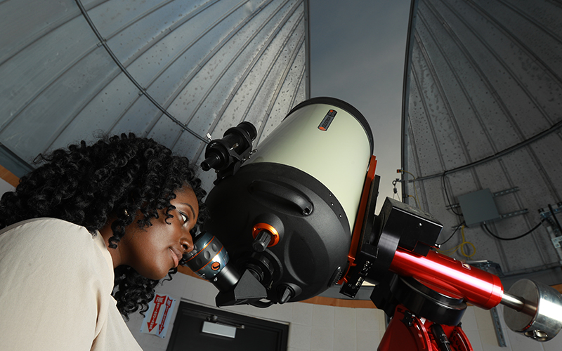 woman looking through a telescope at the sky in an observatory