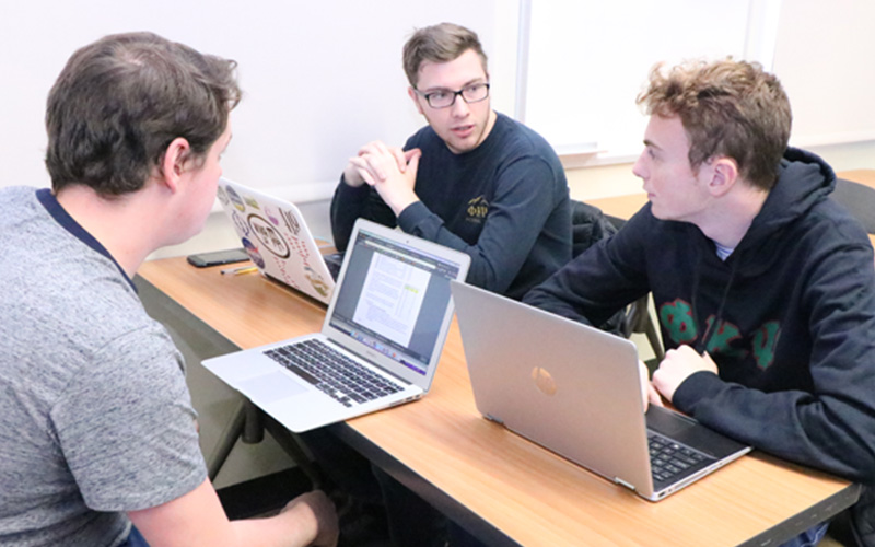 group of students sit together with their laptops open 