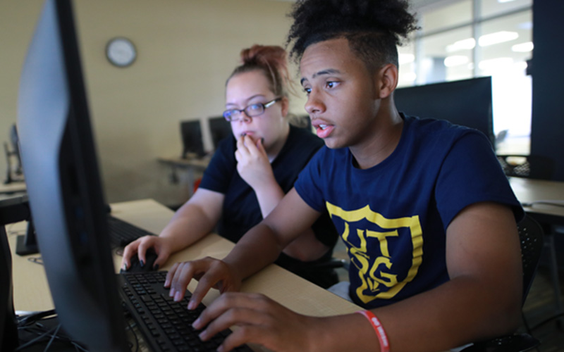 two students sitting in a computer lab share a computer screen