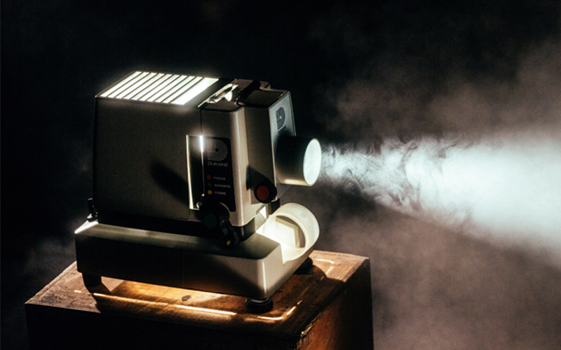 film projector sits on a stand projecting light from its lense in a darkened room