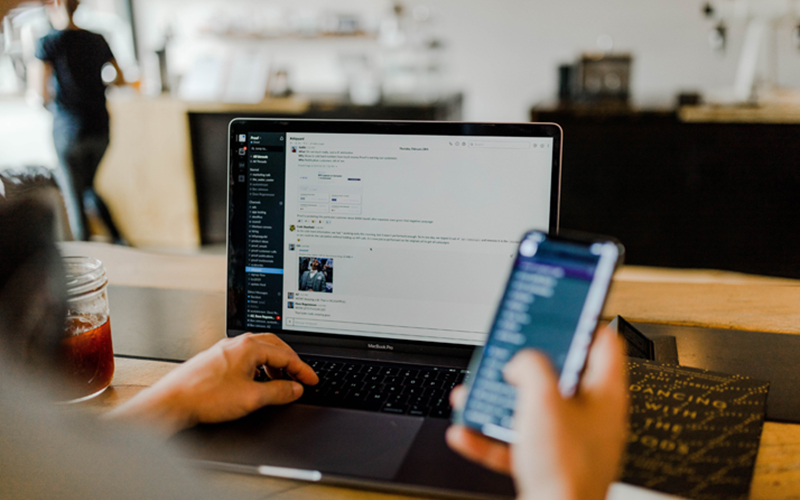 person sitting in front of a laptop simultaneously observes their smart phone screen