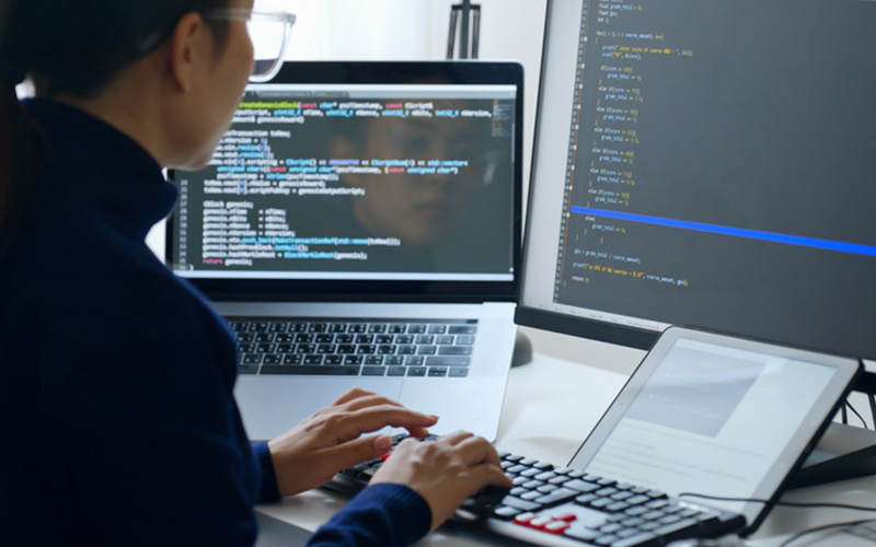 woman sitting in front of two computer monitors with source code displayed on screen