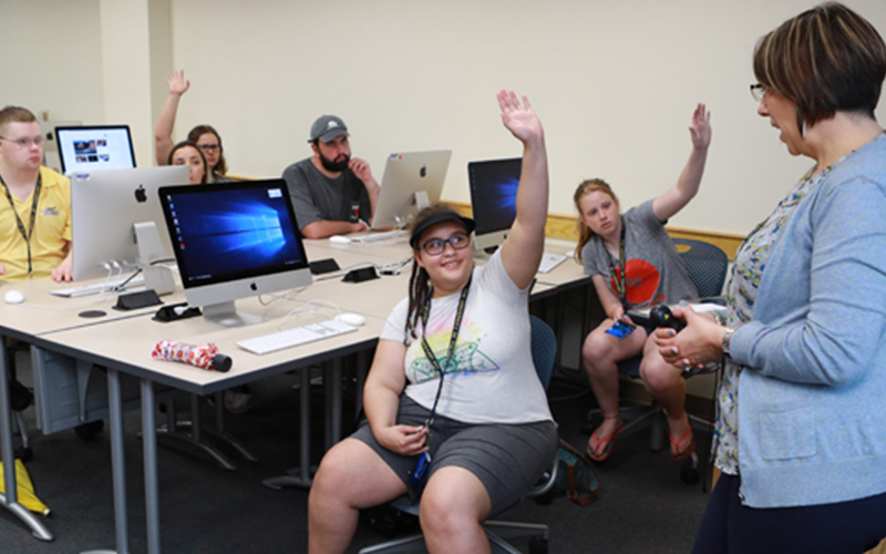 students sitting in a computer lab raise their hand to be chosen by the teacher
