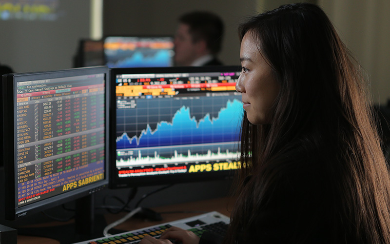 student sits in front of two computer screens and observes the data and charts displayed on the monitors