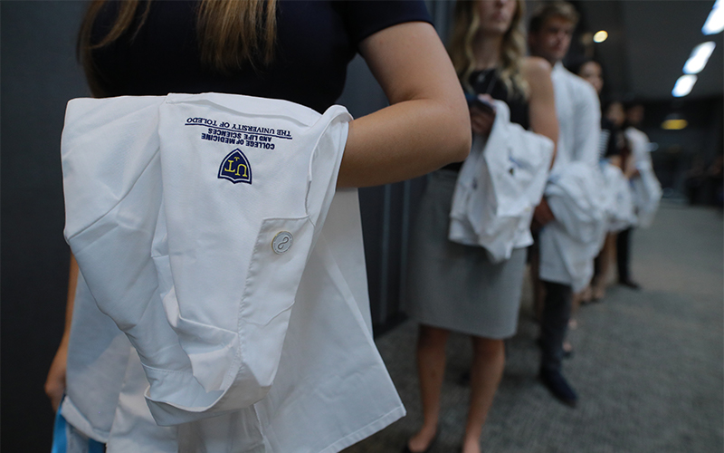 row of medical school graduates holding their UToledo College of Medicine white coats